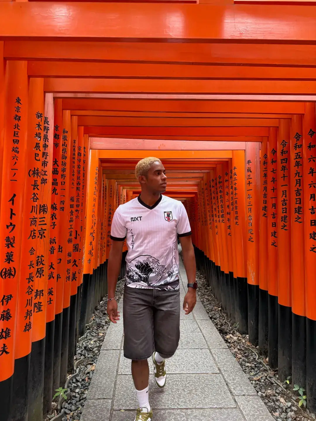 Person wearing NXT JAPAN jersey walking through a traditional orange torii gate pathway.